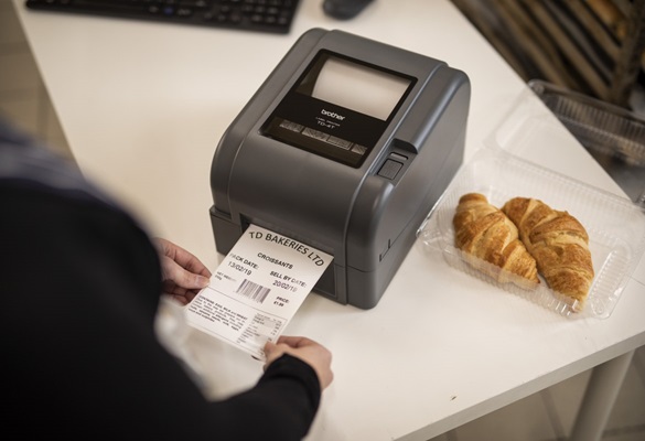Brother címkenyomtató bezárva, amely az étkezési csemege, pékség vagy kávézó hátsó irodájában egy croissant-csomag élelmiszer-napi címkéjét nyomtatja ki.